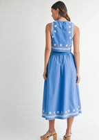 Woman wearing a blue dress with white floral embroidery on a white background