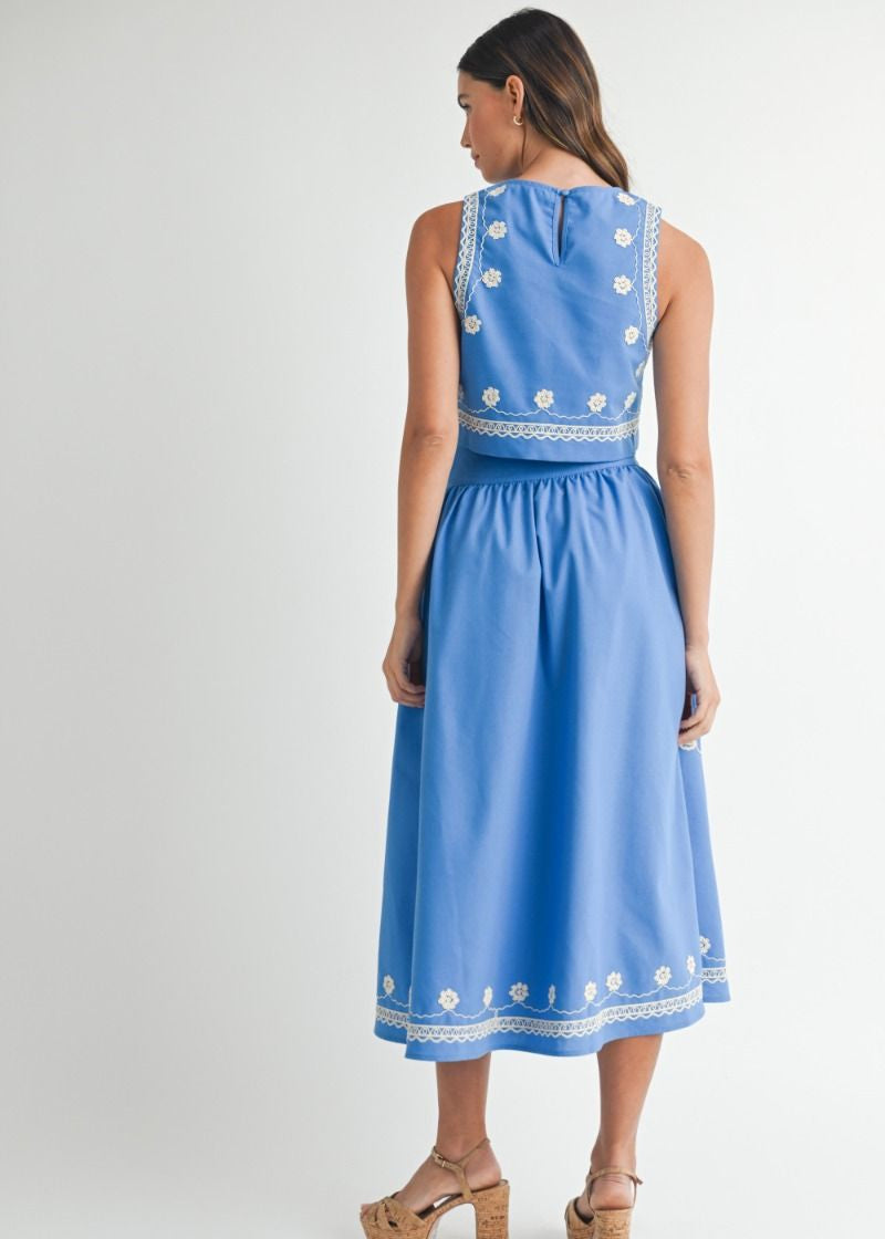 Woman wearing a blue dress with white floral embroidery on a white background