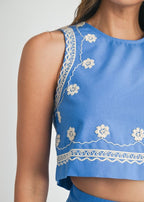 Blue top with white floral embroidery on a plain background